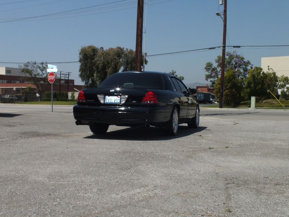 Rear view of black Ford sedan with SVT badge, EVIL VTC California plate and trees behind