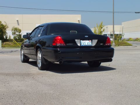 2003 Ford Crown Victoria - Rear-left view of black sedan on open lot, taillights and trunk badge visible