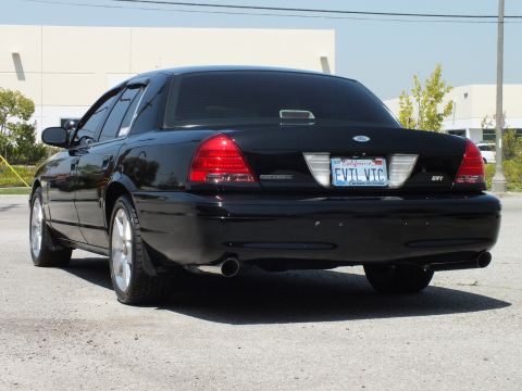 2003 Ford Crown Victoria - Black Crown Victoria from rear-left, chrome wheels and dual exhaust, building behind