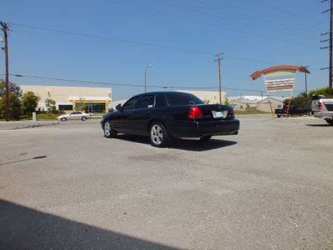 2003 Ford Crown Victoria - Distant rear-left view of black Crown Victoria under blue sky, commercial signage behind