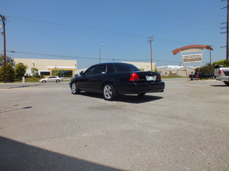 Black full-size Ford sedan rear-quarter parked in lot beside silver car and pickup truck