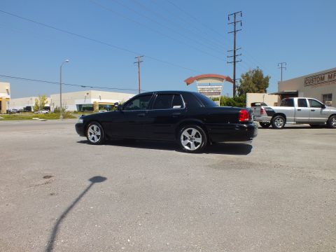 2003 Ford Crown Victoria - Left profile of lowered black Crown Victoria, silver pickup and arched sign behind