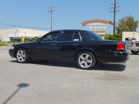 2003 Ford Crown Victoria - Black Crown Victoria left-rear angle on asphalt lot, commercial buildings behind