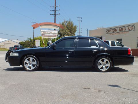 2003 Ford Crown Victoria - Full left profile of lowered black sedan, push bar at front, chrome wheels, signage behind