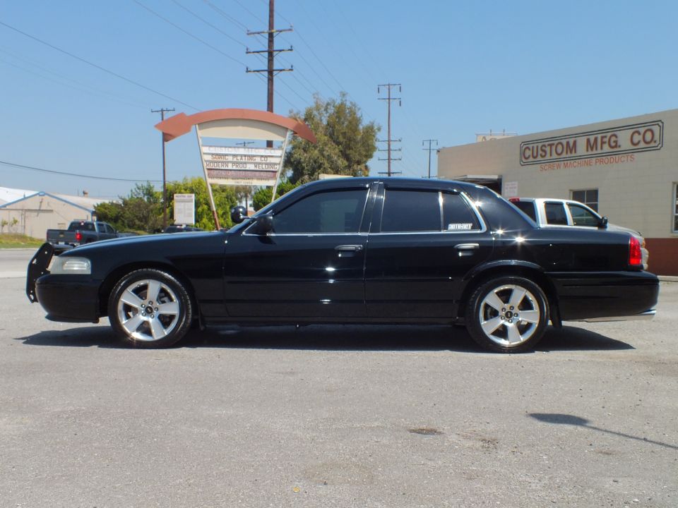 Black Ford Crown Victoria driver-side profile parked outside Custom Mfg Co building