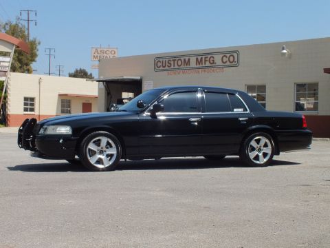 2003 Ford Crown Victoria - Side view of a lowered black Crown Victoria with silver multi-spoke wheels and tinted windows outside an industrial shop