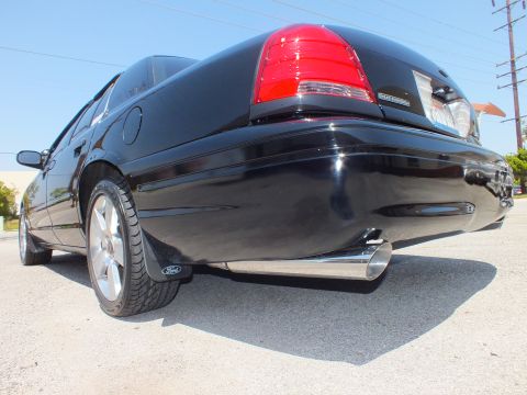 2003 Ford Crown Victoria - Ground-level rear quarter of a black sedan showing taillight, Ford mud flap and chrome exhaust tip