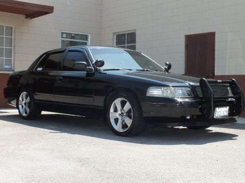 2003 Ford Crown Victoria - Black sedan front quarter showing chrome push bar, side spotlights and silver multi-spoke wheel