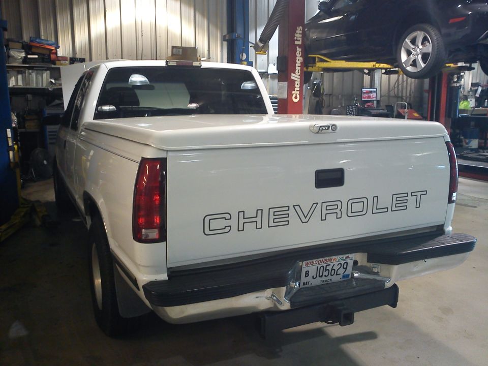 White Chevrolet pickup rear view with tonneau cover and Wisconsin plate in a repair shop