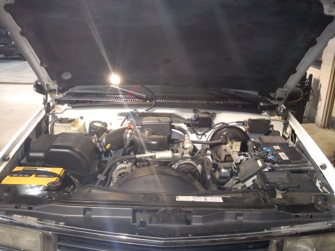 1997 Chevrolet Silverado 1500 - The engine bay of a white 1997 Chevrolet Silverado 1500 is visible with the hood raised, revealing the V8 engine and associated parts.