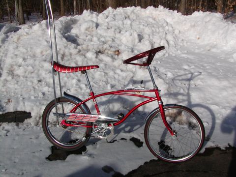 1953 Ford Mainline - A vintage red bicycle with a distinctive sissy bar and a steering wheel is parked in the snow.