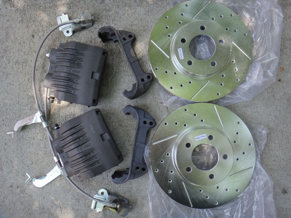 Pair of slotted brake rotors and black calipers with cables on a concrete surface