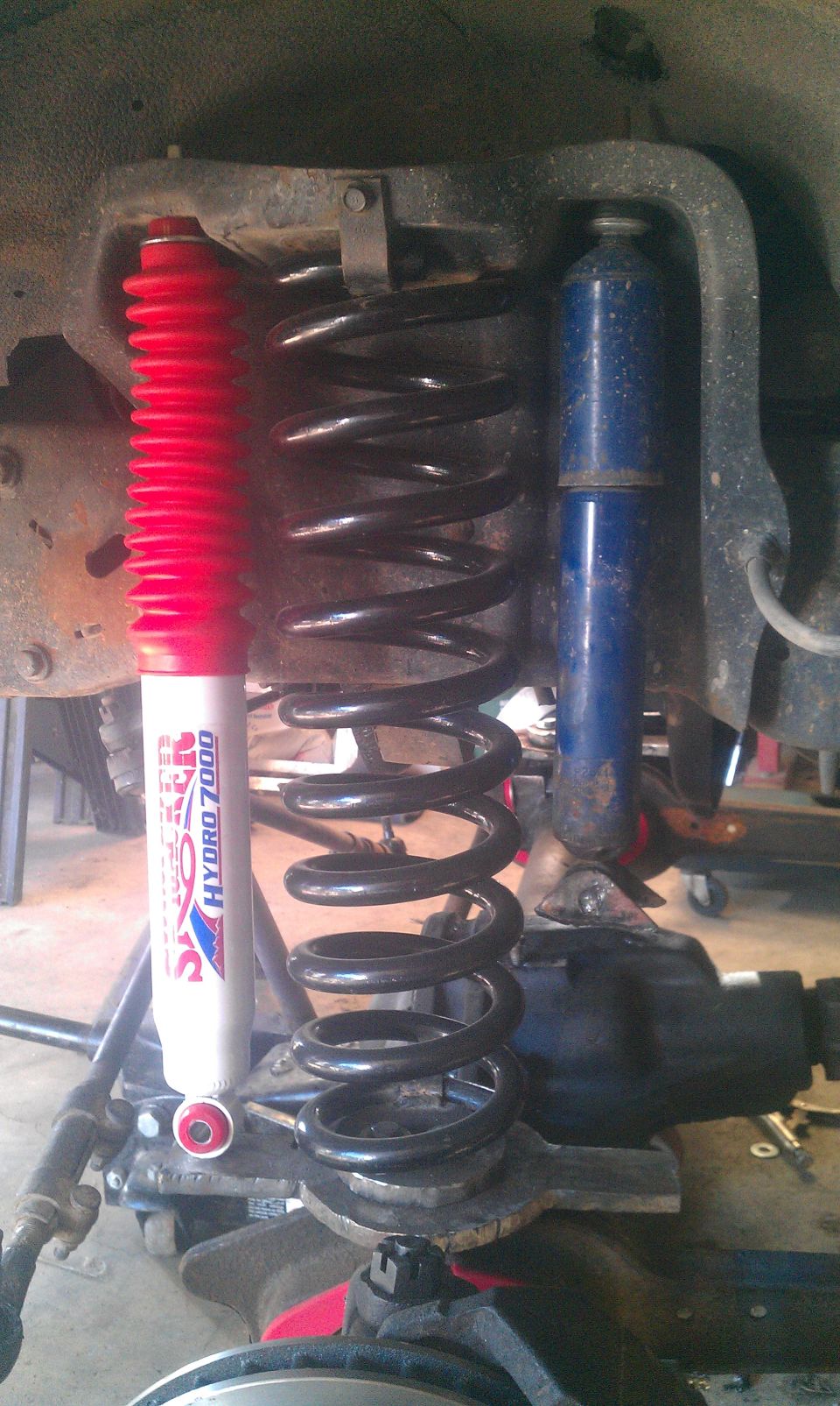Aftermarket red and blue shocks with black coil springs installed on vehicle suspension