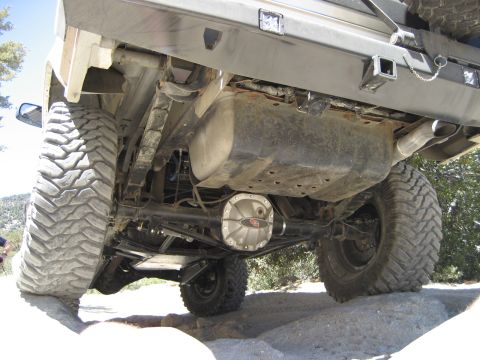 1996 Ford Bronco - The undercarriage of a modified off-road vehicle is shown, with its large tires navigating rocky terrain.