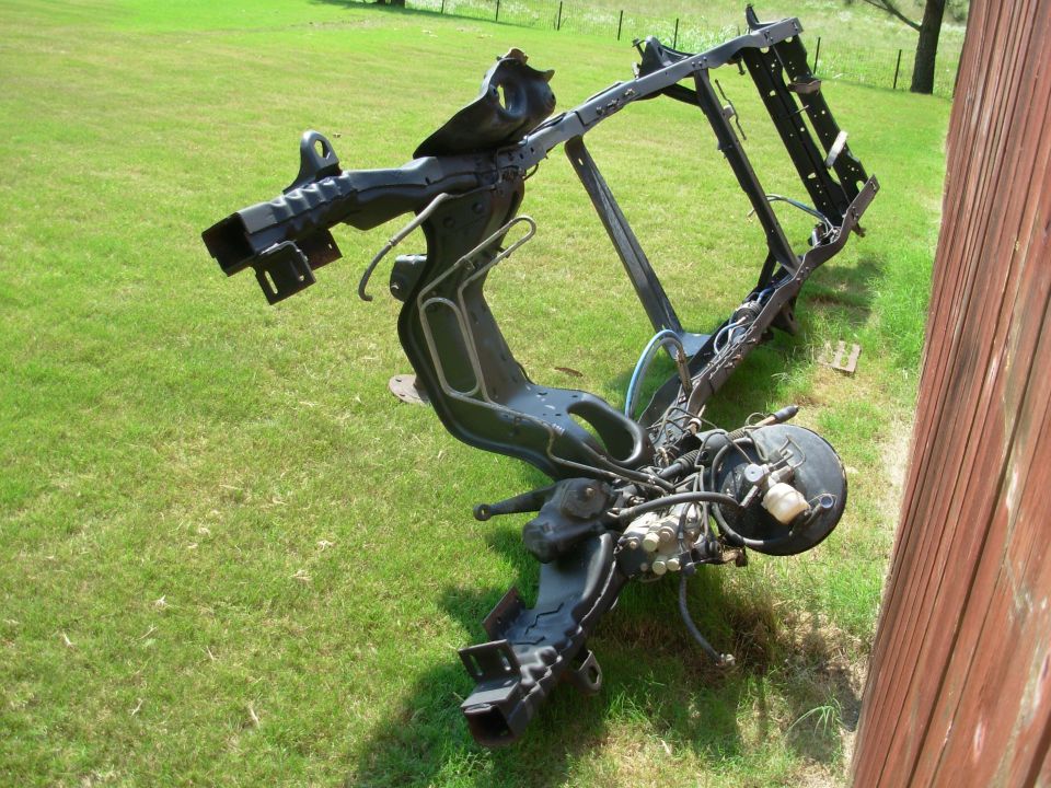 Black-coated bare truck frame with brake booster and lines resting on grass