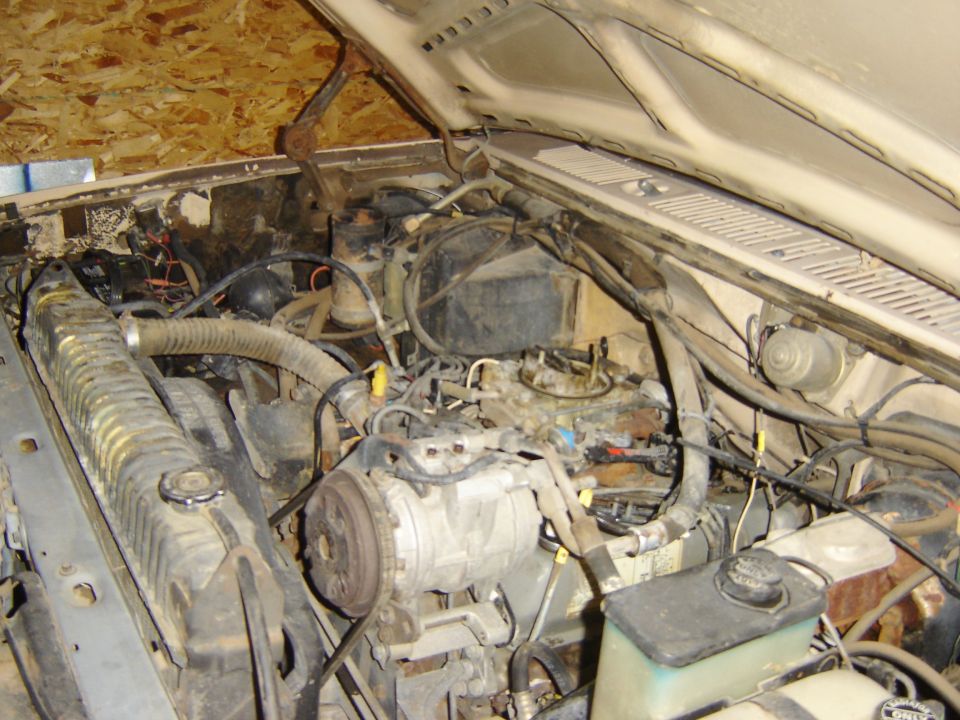 Engine bay with carburetor, radiator, and AC compressor visible. Some wiring and hoses are present