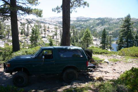 1991 Ford Bronco - A dark green 1992 Ford Bronco is parked off-road with a scenic mountain lake in the background.
