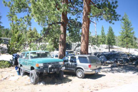 1991 Ford Bronco - A modified green 1991 Ford Bronco sits parked under trees, accompanied by another SUV in a scenic outdoor setting.