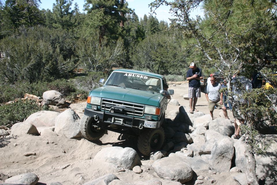 Green 1987 Ford F-150 off-roading over rocks, front view