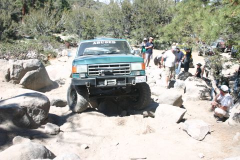 1991 Ford Bronco - This SUV is tackling a challenging off-road course with large rocks and uneven ground.