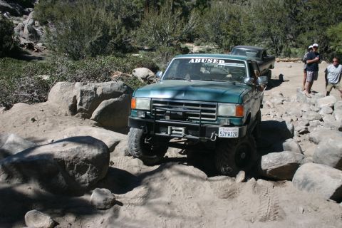 1991 Ford Bronco - A green Ford Bronco navigates a challenging rocky terrain, with another vehicle visible behind it.