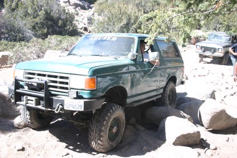 1991 Ford Bronco - This 1991 Ford Bronco is shown off-roading over rocks, with another vehicle visible in the background.