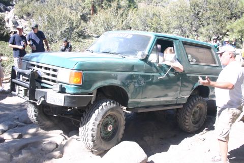 1991 Ford Bronco - This green Ford Bronco is navigating a challenging rocky trail with several people around.