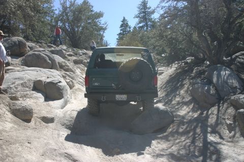 1991 Ford Bronco - A green Ford Bronco tackles a challenging rocky trail with people observing.