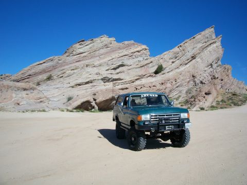 1991 Ford Bronco - A modified green 1991 Ford Bronco sits in a sandy area with large rock formations in the background.