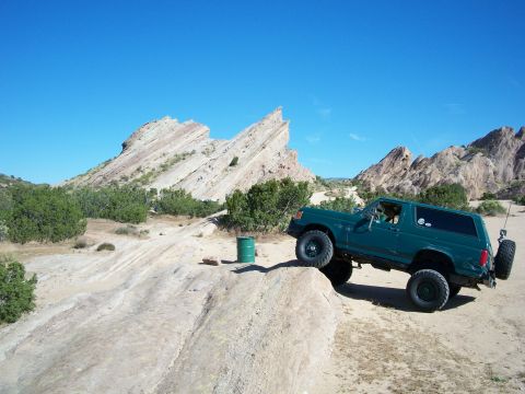 1991 Ford Bronco - Green 1991 Ford Bronco navigating a challenging off-road course with rocky terrain and clear blue skies.