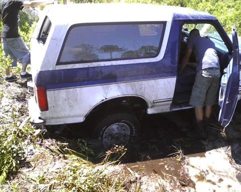 1996 Ford Bronco - A 1996 Ford Bronco is stuck in the mud, with two people attending to it.