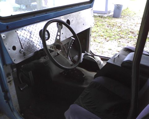 1969 Toyota Land Cruiser - The interior of a vehicle shows a custom dashboard with a steering wheel and seats, with a trash can visible outside.