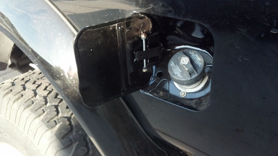 Close-up of a black vehicle's open fuel door, showing the gas cap and tire tread