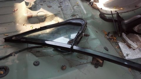 1995 Ford Bronco - The interior of a vehicle shows a disassembled window frame and trim, with the floor exposed and showing signs of wear.