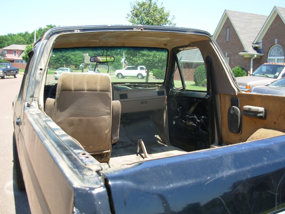 Topless dark blue Bronco interior with tan seat and stripped door, parked in driveway