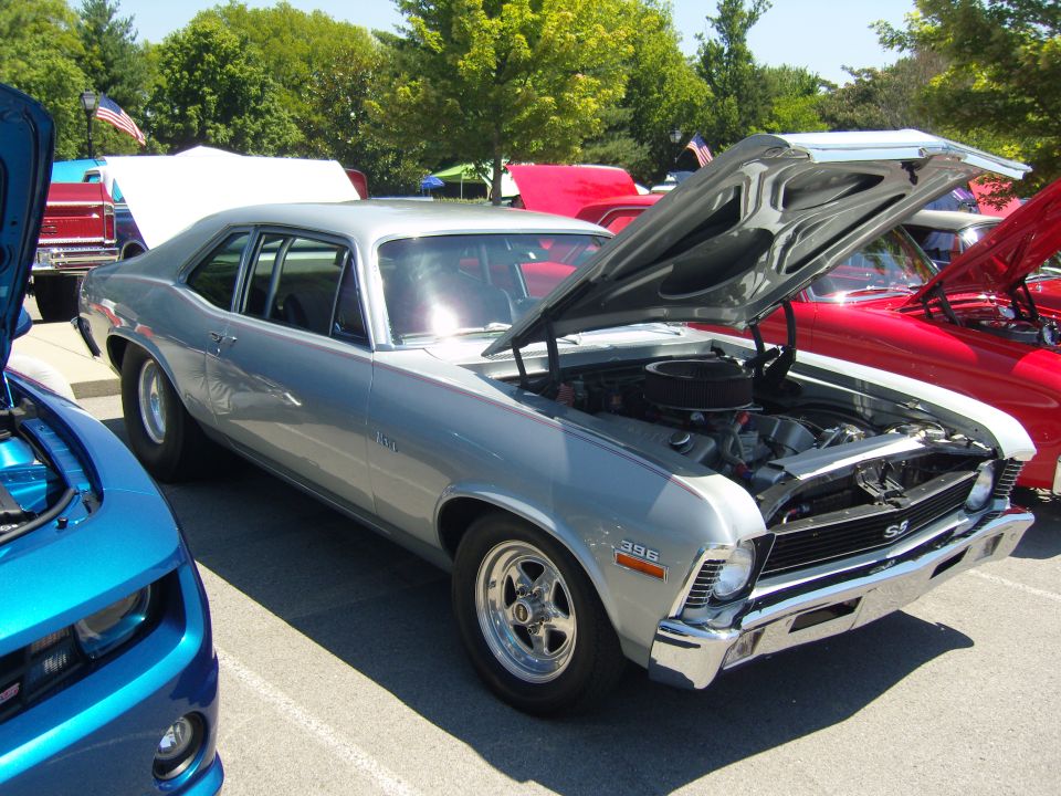 Silver 1969 Chevrolet Nova SS with hood open, parked next to a blue Chevrolet Camaro