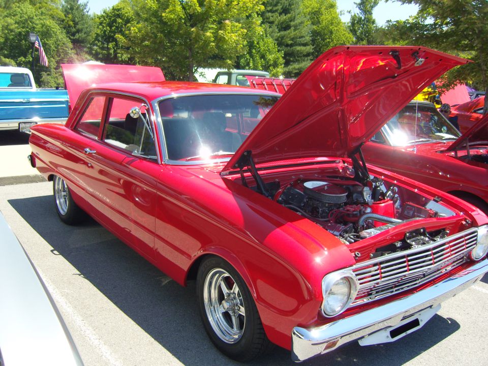 Red sedan with hood open, showing engine. Chrome grille and wheels. Parked outdoors