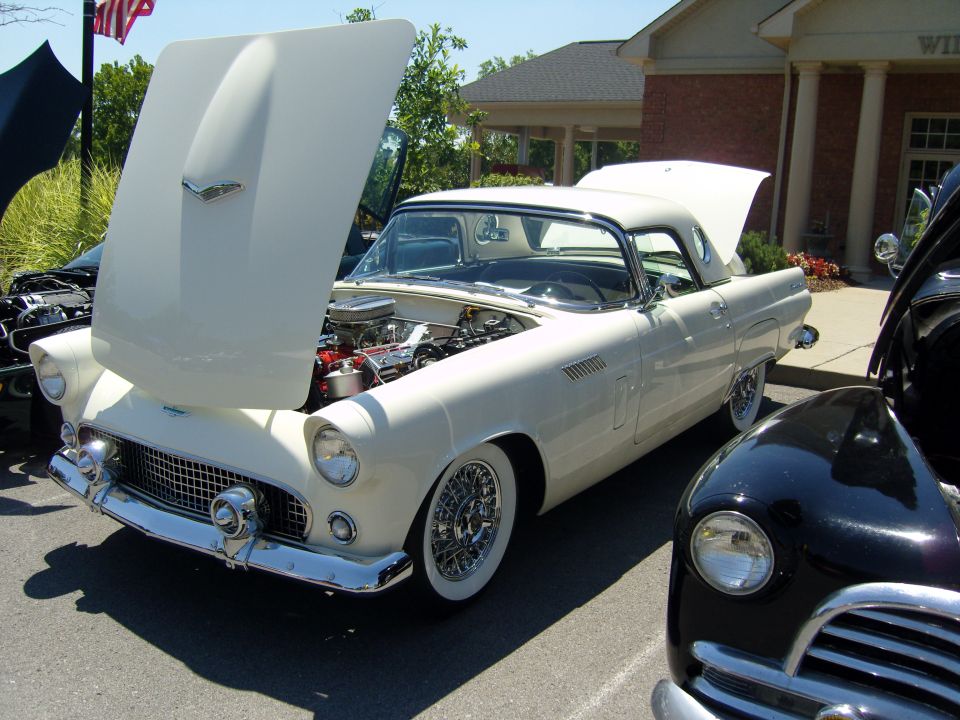 White 1955 Ford Thunderbird convertible with hood and trunk open, wire wheels, parked next to a dark car