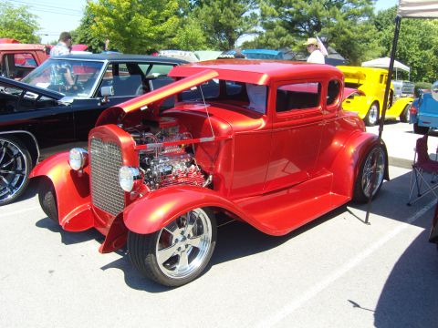 2007 Ford Mustang - A red custom hot rod coupe is parked at an outdoor car show with other vehicles present.