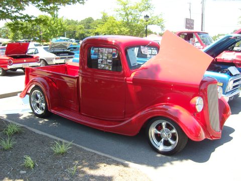 2007 Ford Mustang - A red pickup truck is parked at an outdoor car show with other vehicles visible.