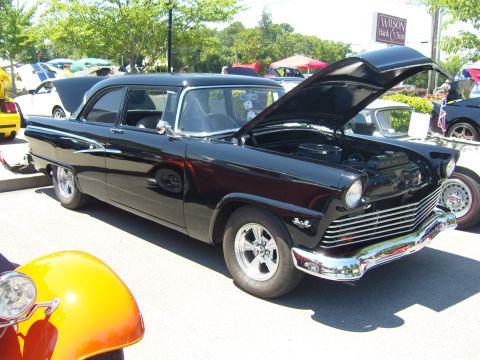 2007 Ford Mustang - A black classic sedan, likely a 1955 model, is displayed with its hood open at a car show. The vehicle features a prominent chrome grille a…