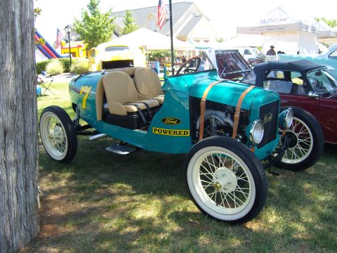 2007 Ford Mustang - A teal antique Ford roadster with tan seats and wire wheels is displayed outdoors next to another vehicle.