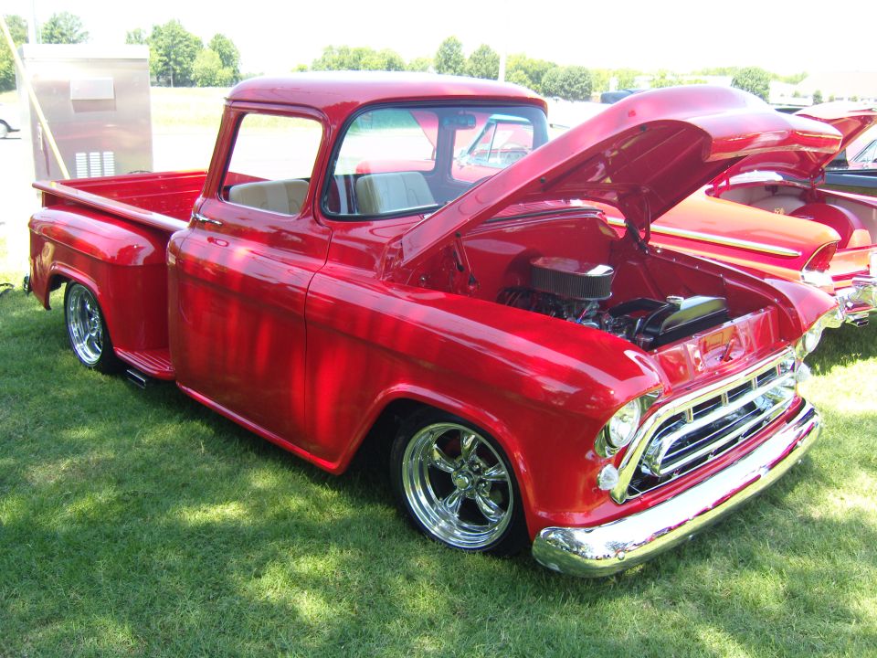 Red pickup truck with hood open, showing engine. Another classic car is parked next to it