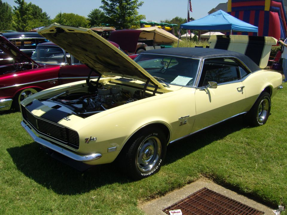 Yellow 1968 Chevrolet Camaro SS with black stripes on hood and trunk, hood open, parked on grass