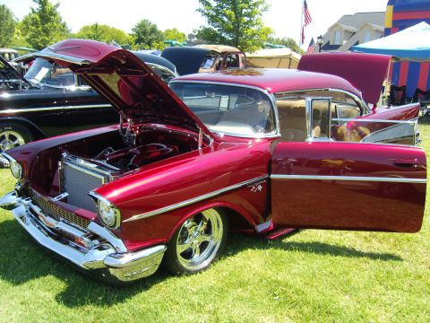 2007 Ford Mustang - A shiny red 1957 Chevrolet Bel Air is displayed with its hood and driver's door open at a car show.