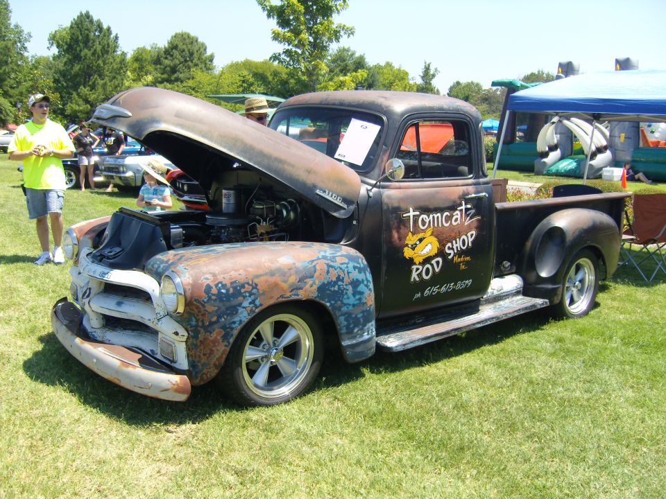 Rusty pickup truck with hood open, "Tomcatz Rod Shop" text on door, custom wheels