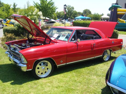 2007 Ford Mustang - A bright red 1966 Chevrolet Nova coupe is displayed with its hood and trunk open at an outdoor car show.