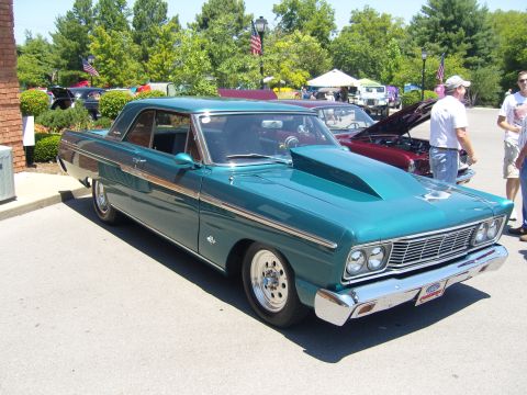 2007 Ford Mustang - A teal 1965 Ford Fairlane coupe is parked at an outdoor event with other vehicles in the background.