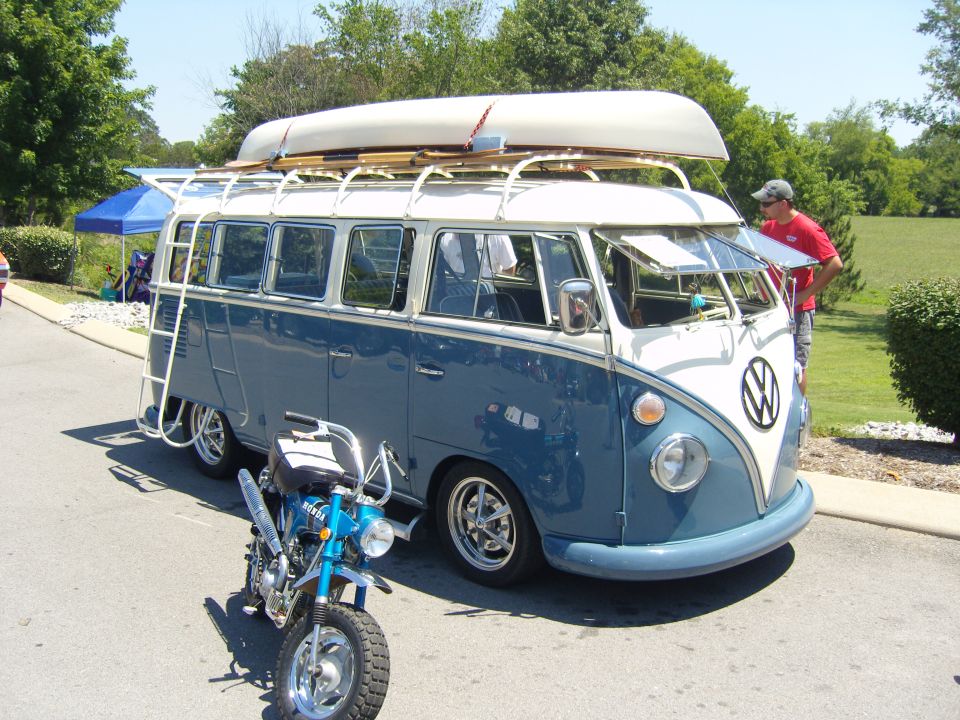 Blue and white Volkswagen bus with canoe on roof, small blue motorcycle parked in front
