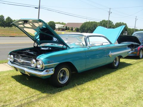 2007 Ford Mustang - A classic teal Chevrolet Impala is displayed with its hood open, parked on a grassy area next to another vehicle.